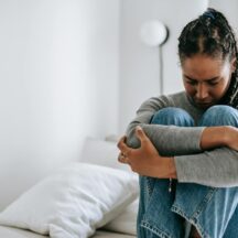 upset ethnic woman embracing knees on bed