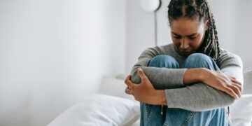 upset ethnic woman embracing knees on bed